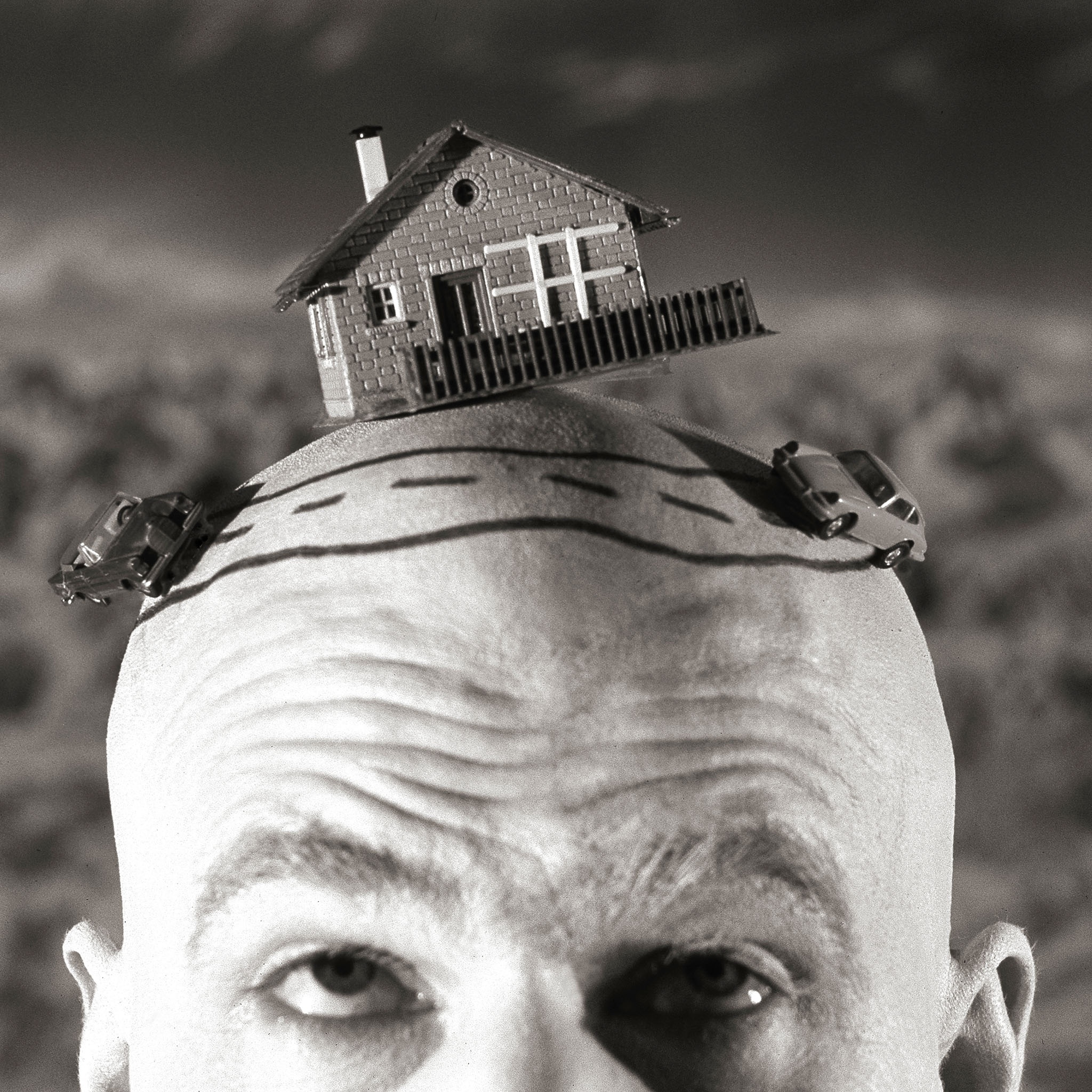 Die-Kurve-Theaterfoto, Mann mit Glatze hat Modelautos und Haus auf dem Kopf