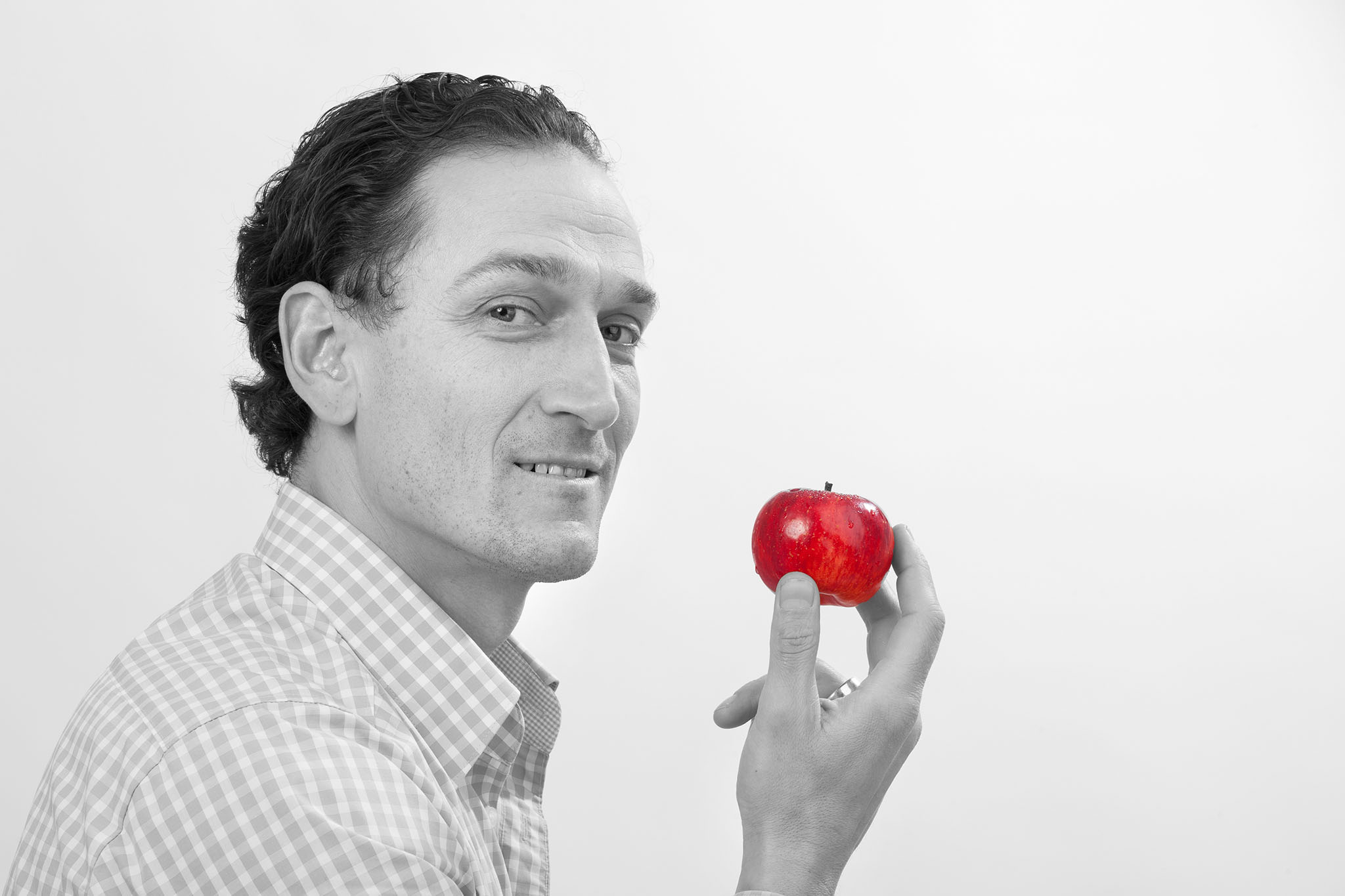 Firmenportrait-Obstlieferant, Mann in SW haelt Apfel (rot) in der Hand